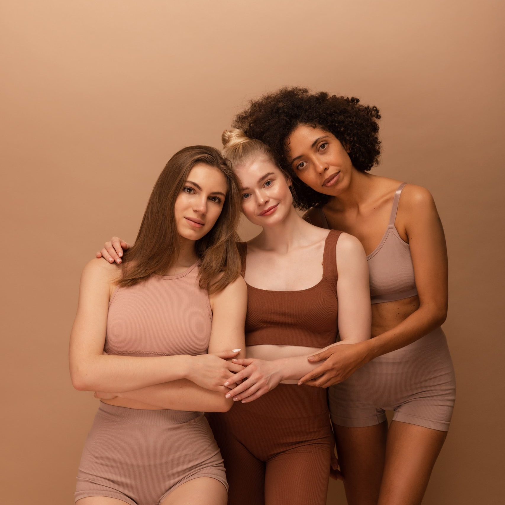pretty-young-women-african-caucasian-appearance-hugging-each-other-looking-camera-beige-background